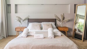 Ein ordentlich bezogenes Bett mit zwei Kissen, ein Nachttisch mit einer Pampasgras-Vase und ein Spiegel an der Wand.