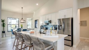 A modern kitchen with white cabinets, stainless steel appliances, and a central island with bar stools. - Villa Serenity - newly built on water, pool & spa (Cape Coral)
