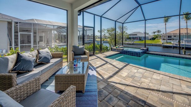 A sunlit outdoor patio with a pool, wicker furniture, and a glass enclosure. - Villa Serenity - newly built on water, pool & spa (Cape Coral)
