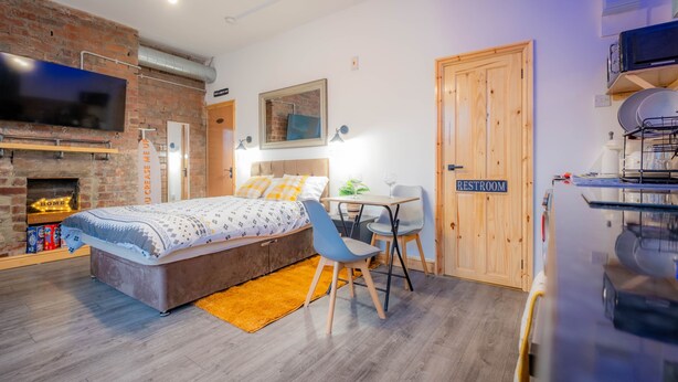 Un dormitorio moderno con pared de ladrillo, una cama, un escritorio y un televisor.