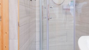 Un baño moderno con cabina de ducha de vidrio, un lavabo blanco y suelo de baldosas.