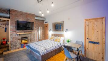 A modern bedroom with a brick fireplace, a bed, a desk, and a chair.