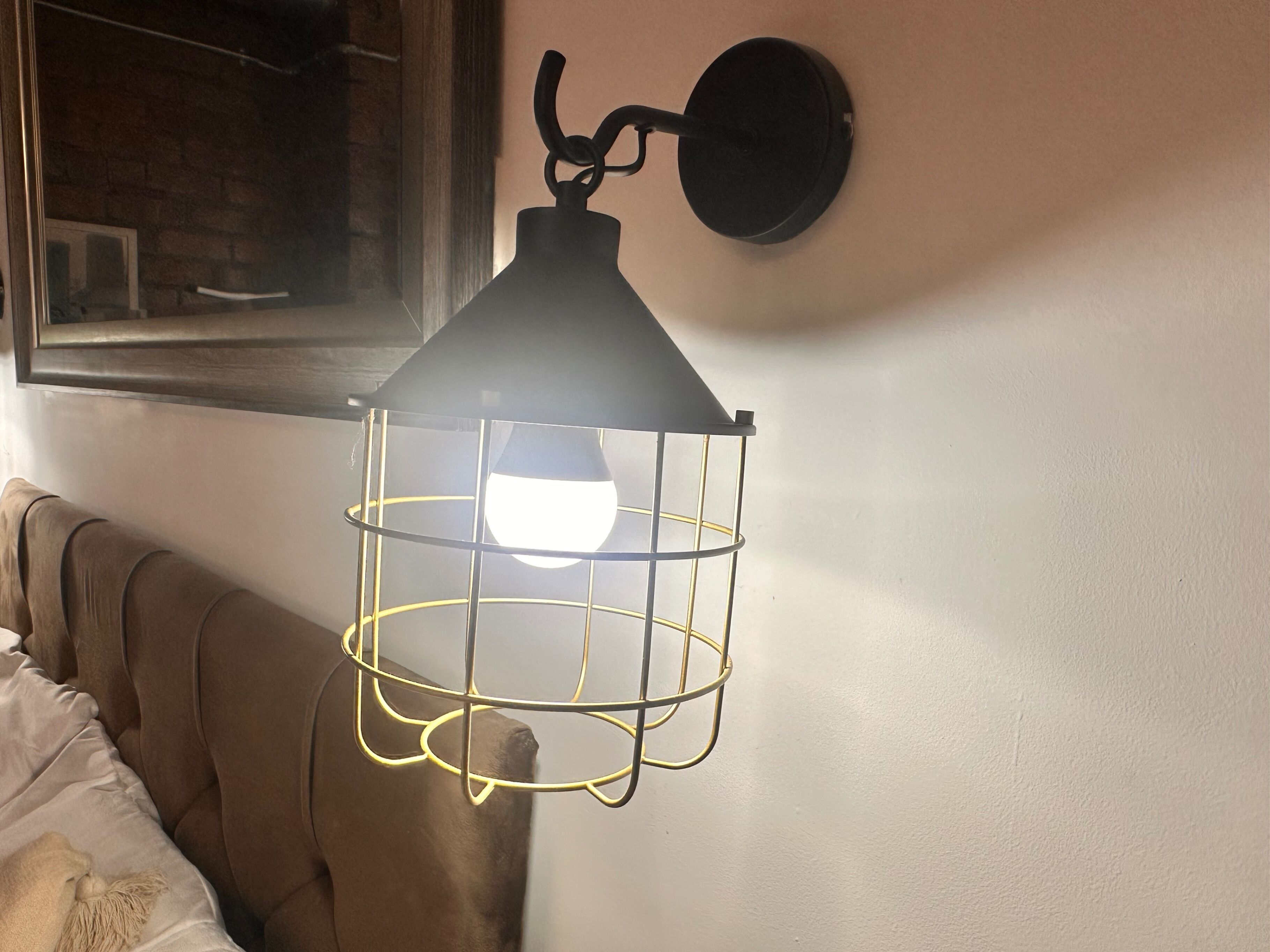 Un luminaire suspendu, doté d’une armature métallique et d’une ampoule à l’intérieur, fixé au mur.