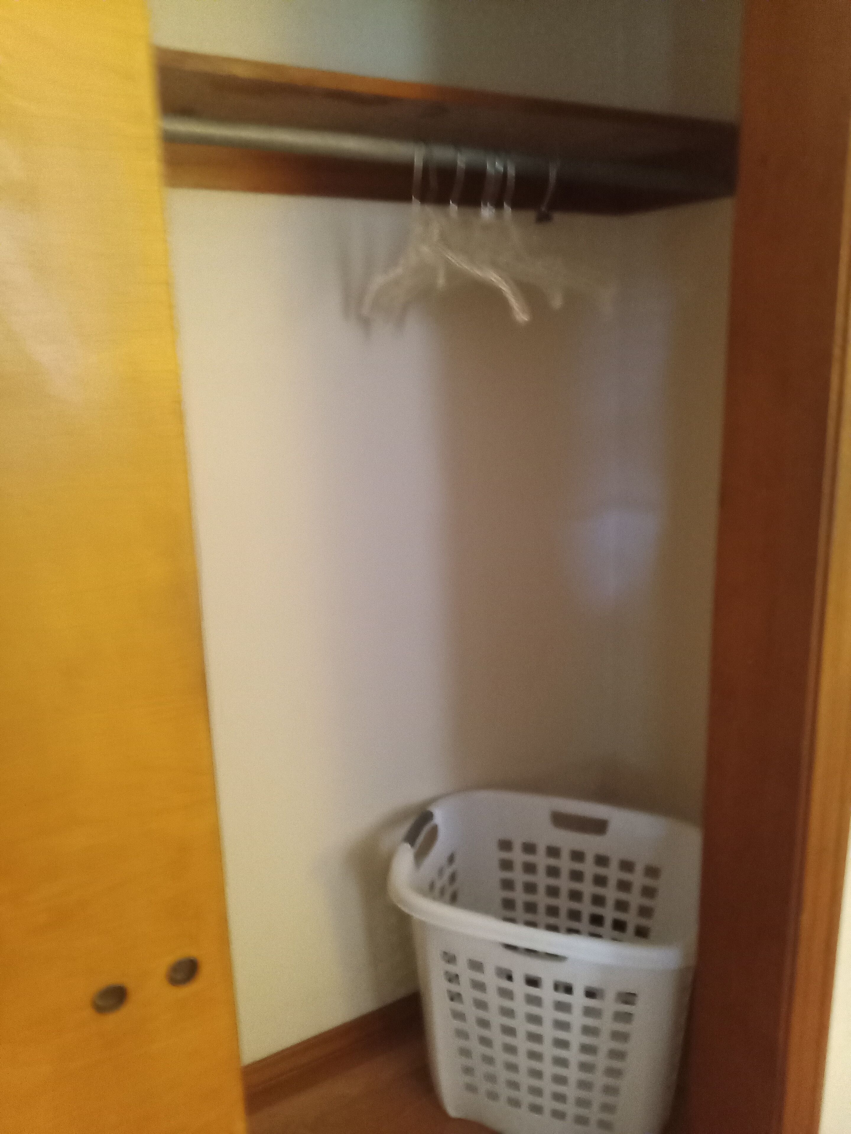 Una cesta de ropa en un rincón de una habitación con suelo de madera y pared blanca.