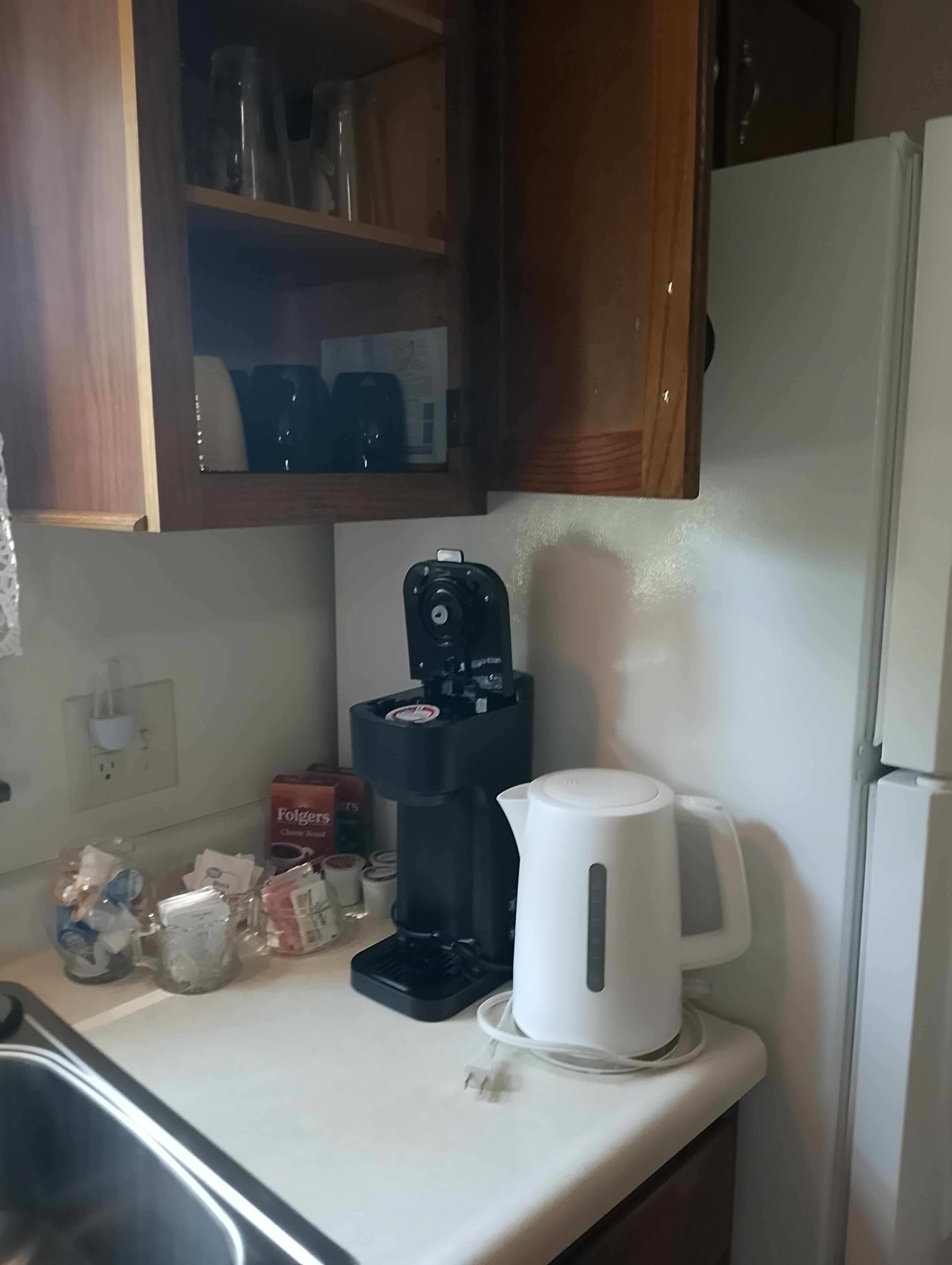 A kitchen with a coffee maker, a kettle, and a box of Folgers coffee.