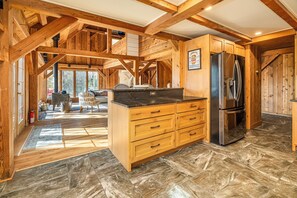 Une cuisine rustique avec des poutres en bois, un grand réfrigérateur et un sol carrelé en pierre.