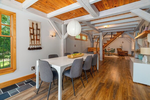 Un espace repas avec une table blanche et des chaises grises, un plafond en bois et un escalier menant à un autre niveau.