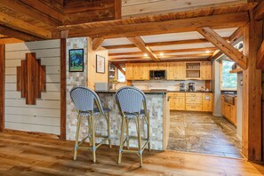 A rustic kitchen with wooden beams, a tiled backsplash, and a bar area with two chairs. - Wood Stove, Pool Table & Lake Dock (Goreville)
