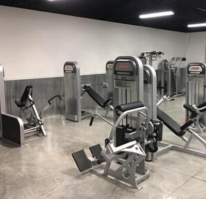 Une salle de sport équipée de divers appareils d’exercice, notamment des bancs de musculation et des appareils de cardio.