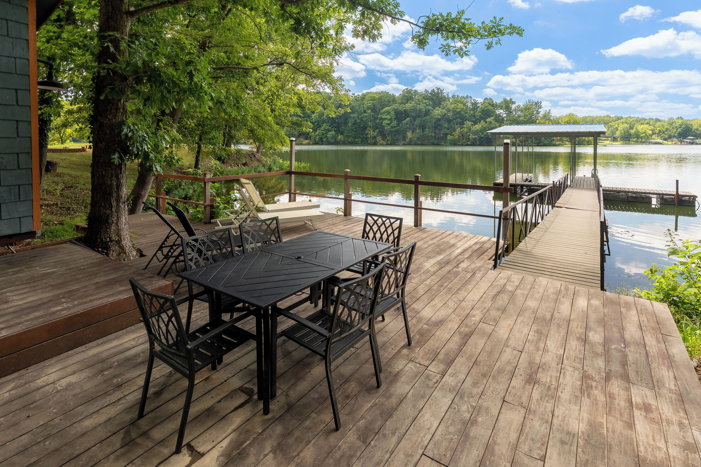 Une terrasse en bois avec une table et des chaises, donnant sur un lac paisible, avec un quai et un pavillon.