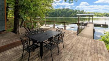 Une terrasse en bois avec une table et des chaises, donnant sur un lac paisible, avec un quai et un pavillon.