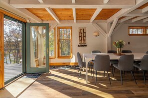 Un espace repas doté d’un plafond en bois, de grandes fenêtres et d’une vue sur les arbres.