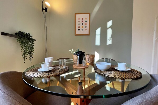 A round glass table with white cups and a small vase, surrounded by woven placemats and a hanging plant. - Elegant apt in Historical Building (Milan)