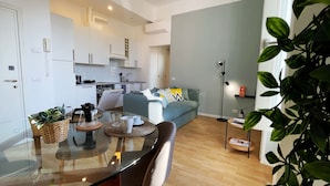 A modern kitchen with white cabinets, a dining table with chairs, and a sofa in the living area.