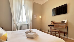 A hotel room with a large bed, a desk with a chair, a flat-screen TV, and a window with curtains.