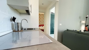 A modern kitchen with a built-in stove, a sink, and a green sofa in the adjacent living area.