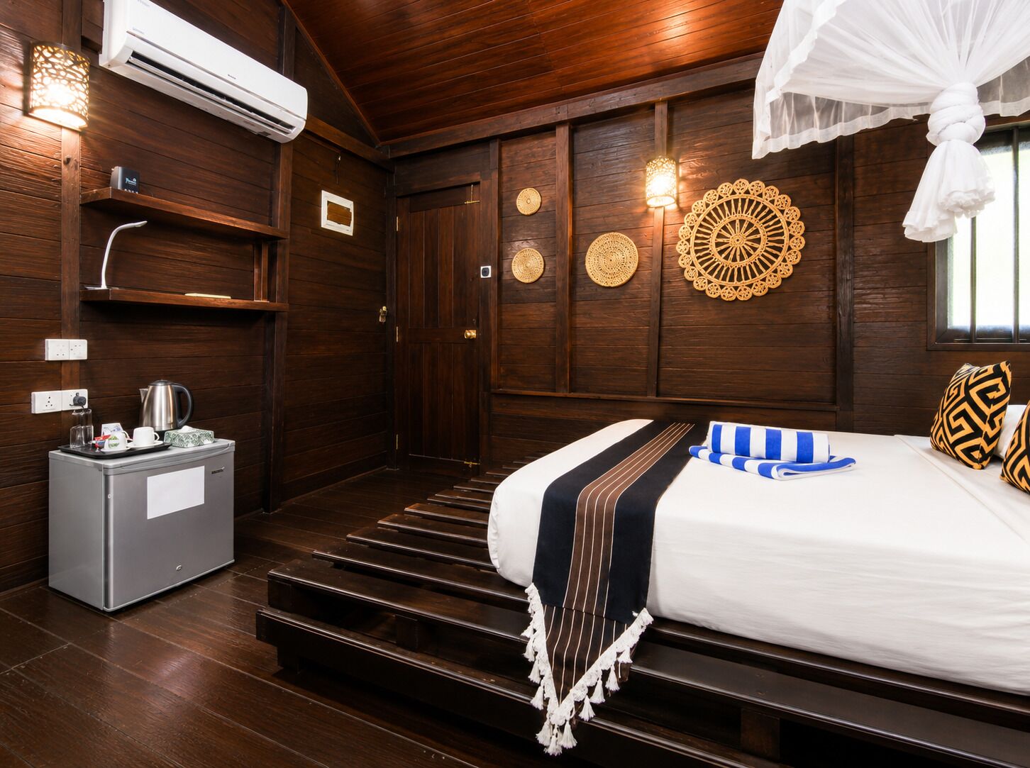 A hotel room with a bed, a minibar, a wall-mounted air conditioner, and decorative wall panels.