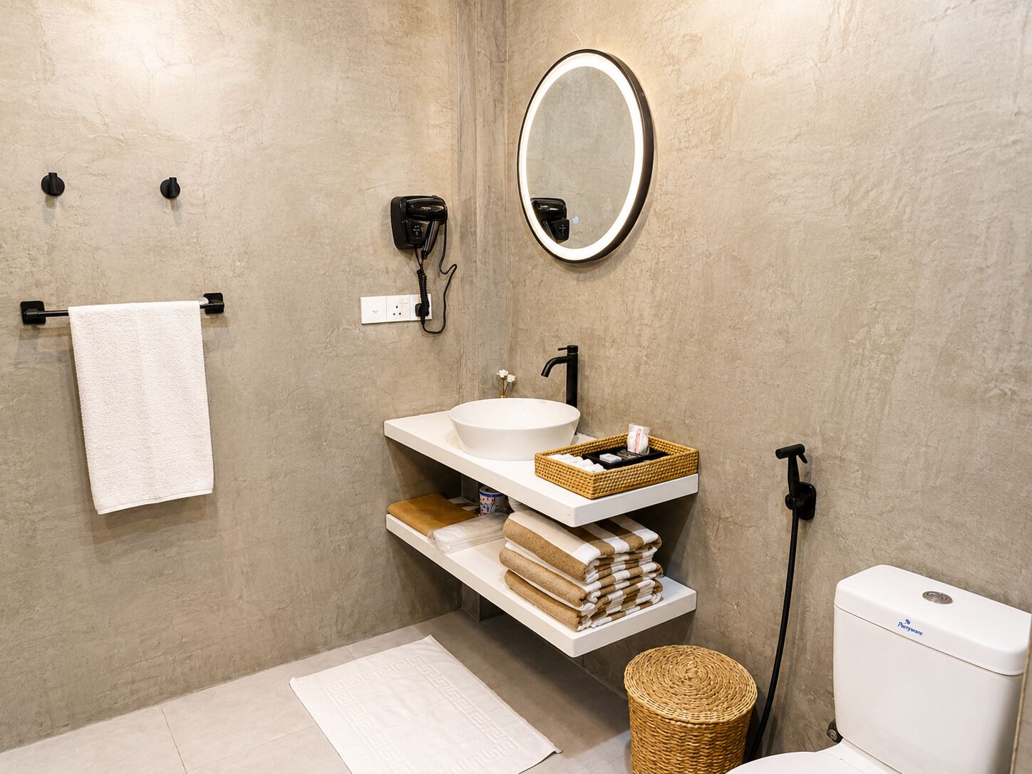A modern bathroom with a white sink, a round mirror, a towel rack, and a toilet.