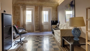Une pièce avec un sol à carreaux, un canapé, un fauteuil, une lampe et un téléviseur.