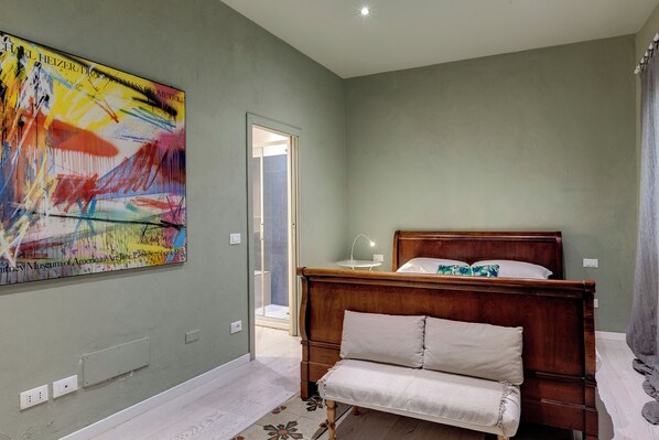 A bedroom with a wooden bed, a bench, a large abstract painting, and a door leading to a bathroom. - Mamo Florence - Orto Apartment (Florence)
