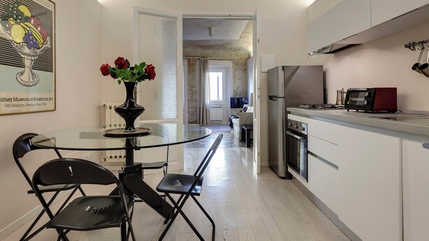 Une cuisine moderne avec une table à manger en verre, des chaises noires et un vase rempli de fleurs rouges.