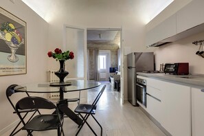 Una cocina moderna con una mesa de vidrio, sillas negras y un florero con flores rojas.