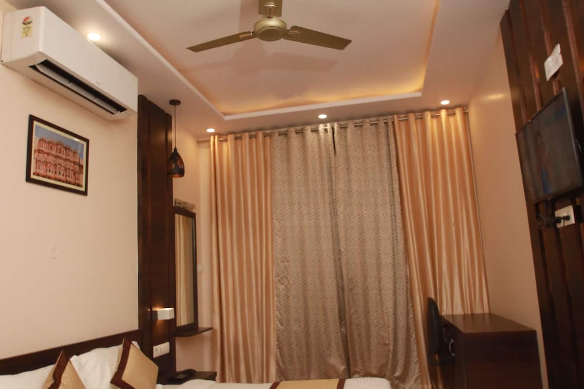 Ein Hotelzimmer mit Bett, Schreibtisch, Deckenventilator, Klimaanlage, Fernseher und Vorhängen.