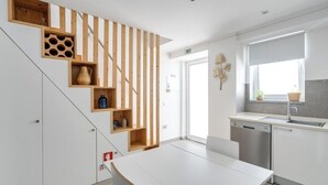 Une cuisine moderne avec des meubles blancs, un escalier en bois doté d’étagères intégrées et une fenêtre offrant une belle vue.
