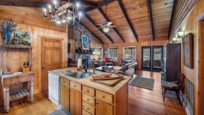 A rustic cabin interior with a wooden interior, a kitchen with a sink and cabinets, a dining area with a table and chairs, and a stone fireplace. - Lake Lahusage Front l Private Dock, Game Room (Mentone)
