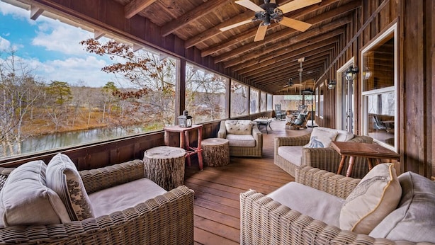 A covered outdoor seating area with wicker furniture, a ceiling fan, and large windows overlooking a natural landscape. - Lake Lahusage Front l Private Dock, Game Room (Mentone)