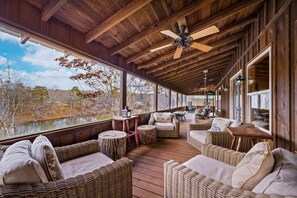 A covered outdoor seating area with wicker furniture, a ceiling fan, and large windows overlooking a natural landscape. - Lake Lahusage Front l Private Dock, Game Room (Mentone)