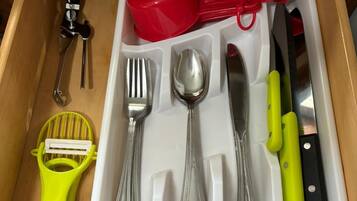 A drawer with a utensil organizer containing a red measuring cup, a red spatula, a yellow grater, a knife, a spoon, a fork, and a pair of tongs.
