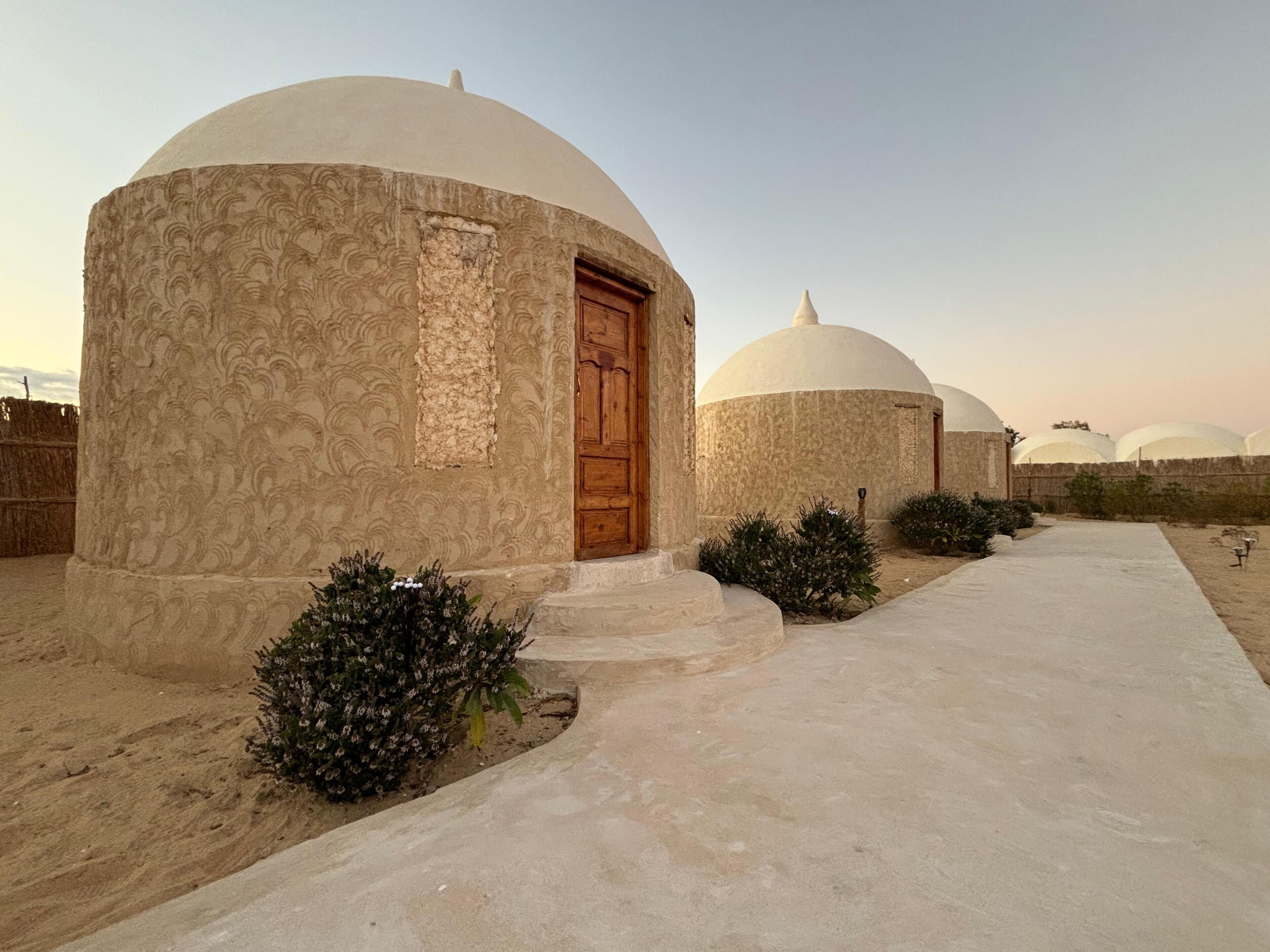 A row of dome-shaped structures with a central door, surrounded by small bushes and a concrete pathway.