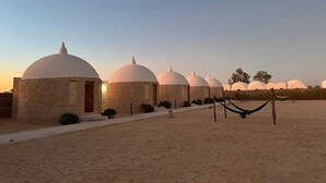 A row of dome-shaped buildings with a sandy ground, a hammock, and a clear sky. - Gazrashek Siwa Eco Lodge (Siwa)