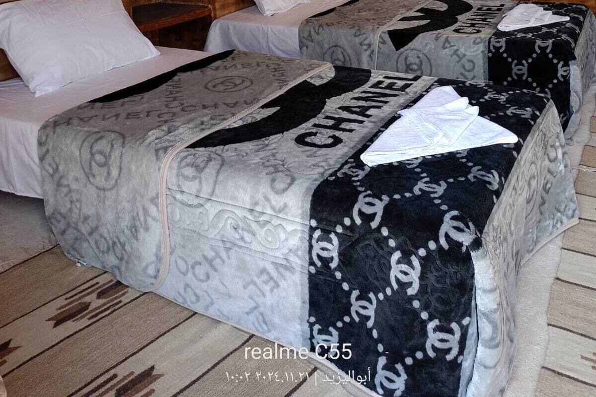 Ein Zimmer mit zwei Betten, jedes mit einer Bettdecke im Chanel-Design, einer Ziegelwand, einer Holztür und einer an der Wand befestigten Lampe.