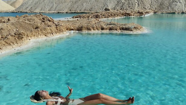 A person floating in clear turquoise water with a rocky landscape in the background. - Gazrashek Siwa Eco Lodge (Siwa)