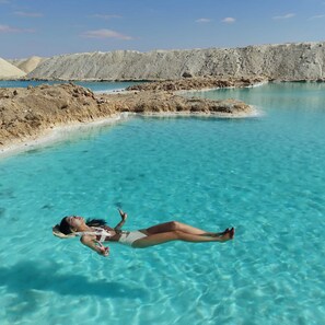 A person floating in clear turquoise water with a rocky landscape in the background. - Gazrashek Siwa Eco Lodge (Siwa)
