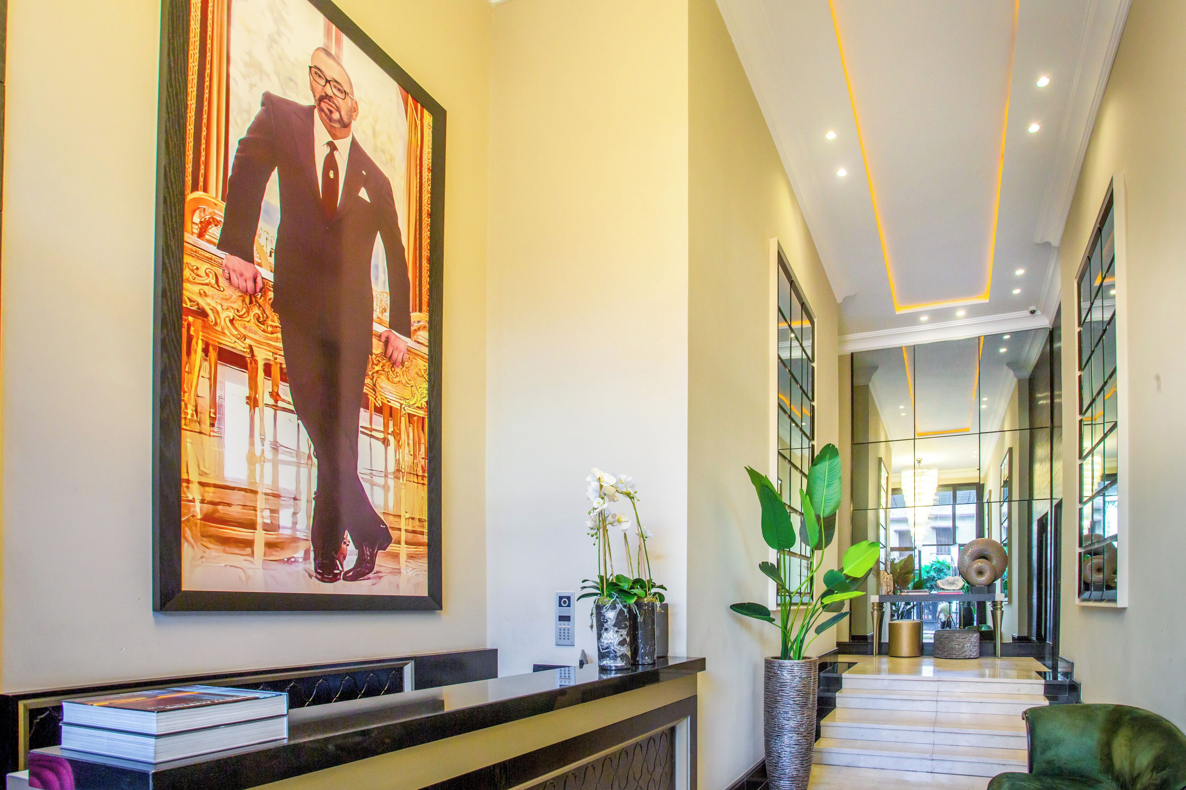 En moderne hotellobby med reception, et stort indrammet kunstværk, en trappe og en potteplante.