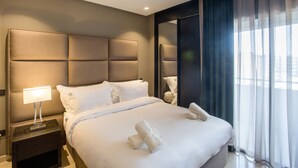 A hotel room with a large bed, a nightstand with a lamp, and a view of the city through sheer curtains. - W-Aldorf (Casablanca)