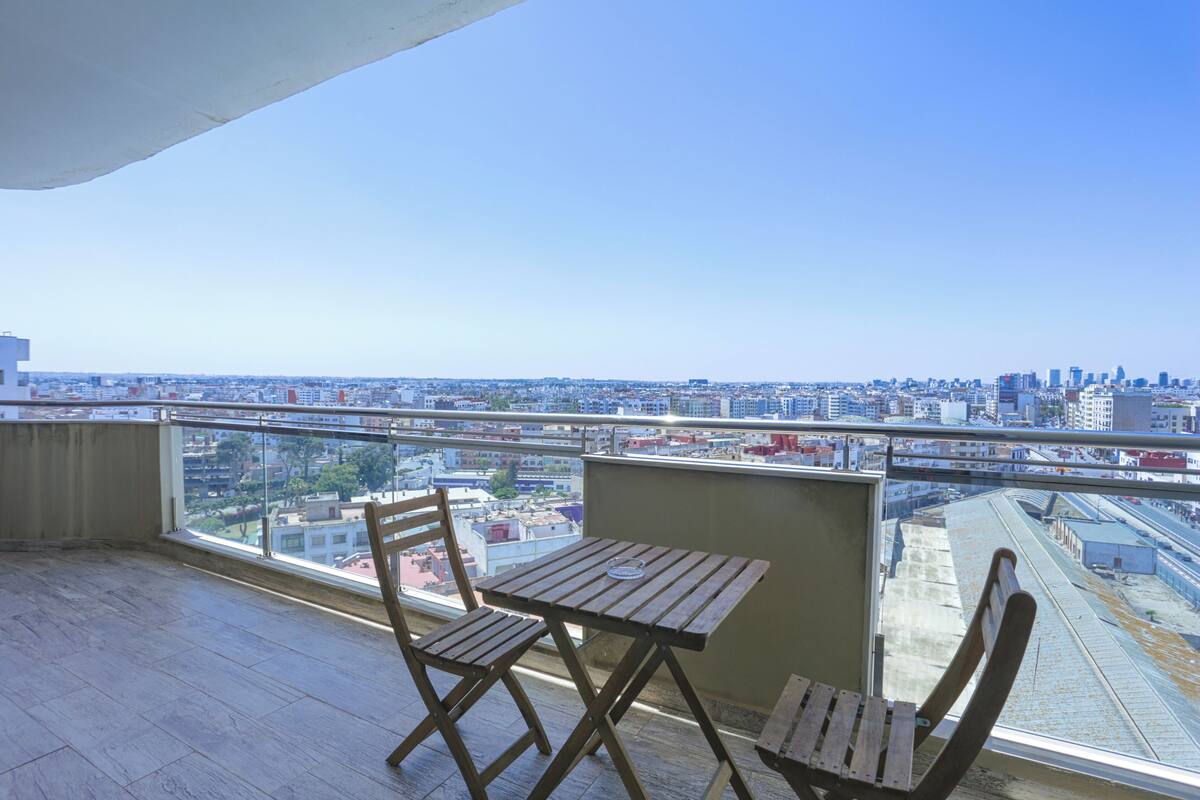 Ein Balkon mit Holztisch und Stühlen, der Blick auf die Stadt bietet.