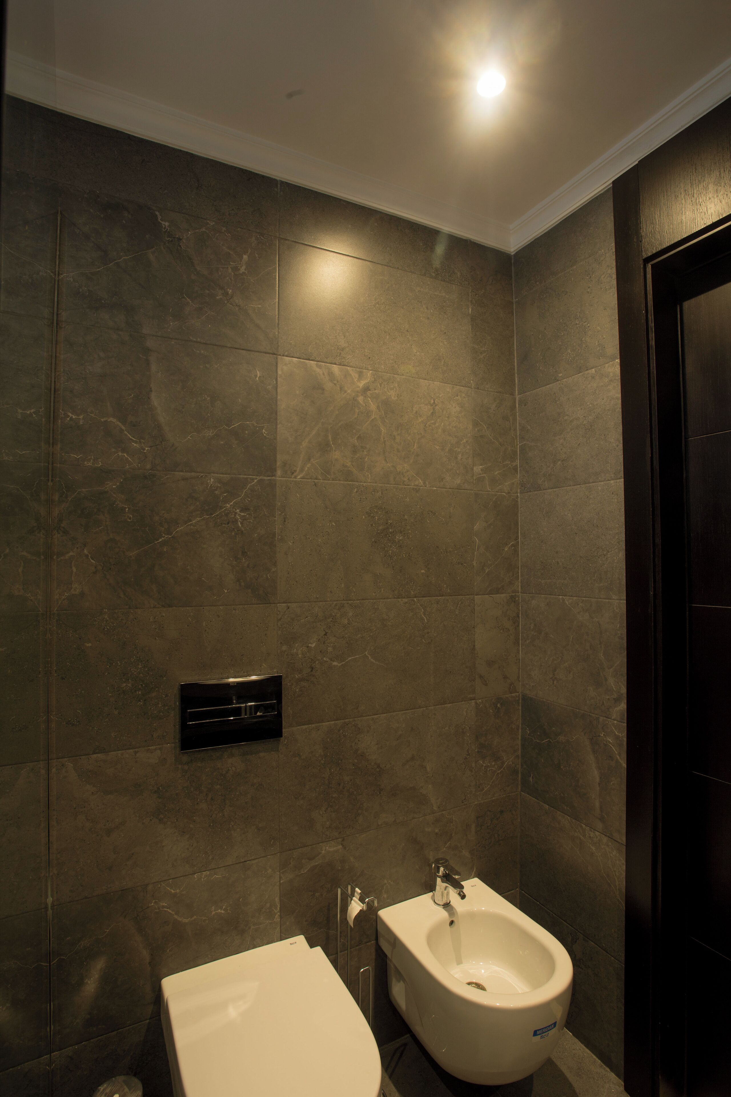 A bathroom with a bidet, a wall-mounted heater, and a dark door.