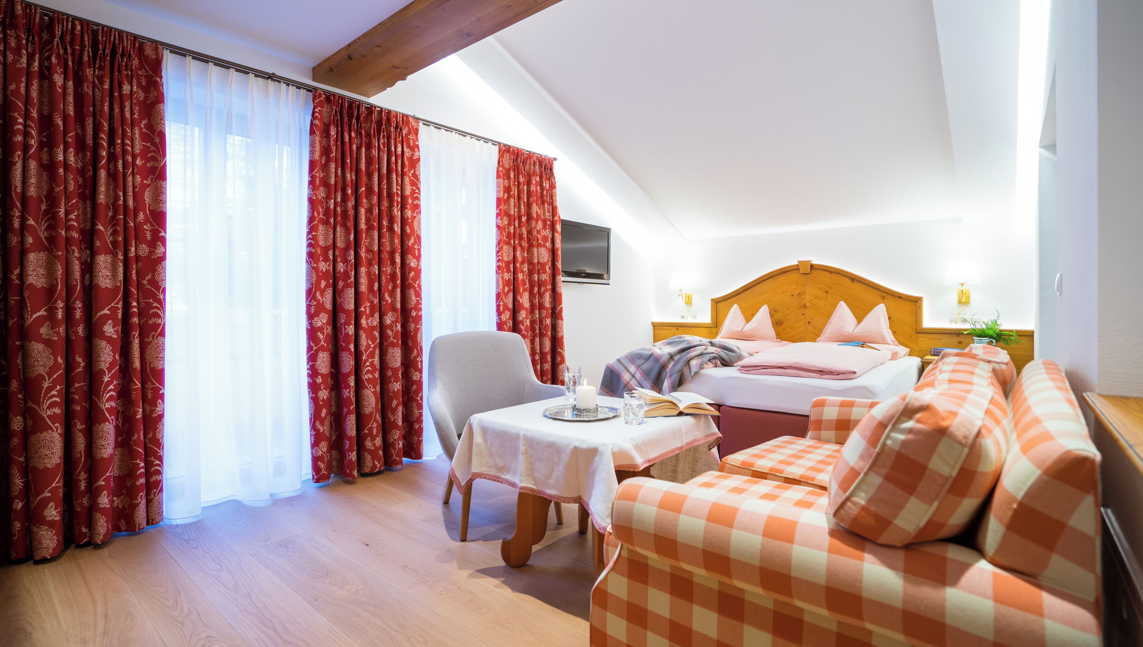 A hotel room with a bed, a sofa, a table with a candle, and curtains.