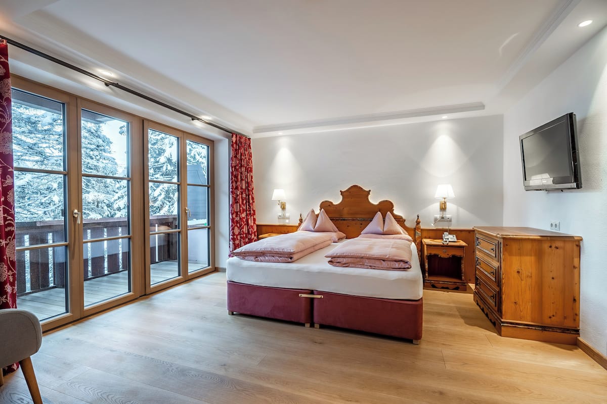 A bedroom with a large bed, a wooden dresser, a television, and a sliding glass door leading to a balcony.