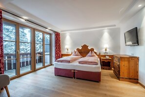A bedroom with a large bed, a wooden dresser, a television, and a sliding glass door leading to a balcony. - Hotel Lech (Lech am Arlberg)