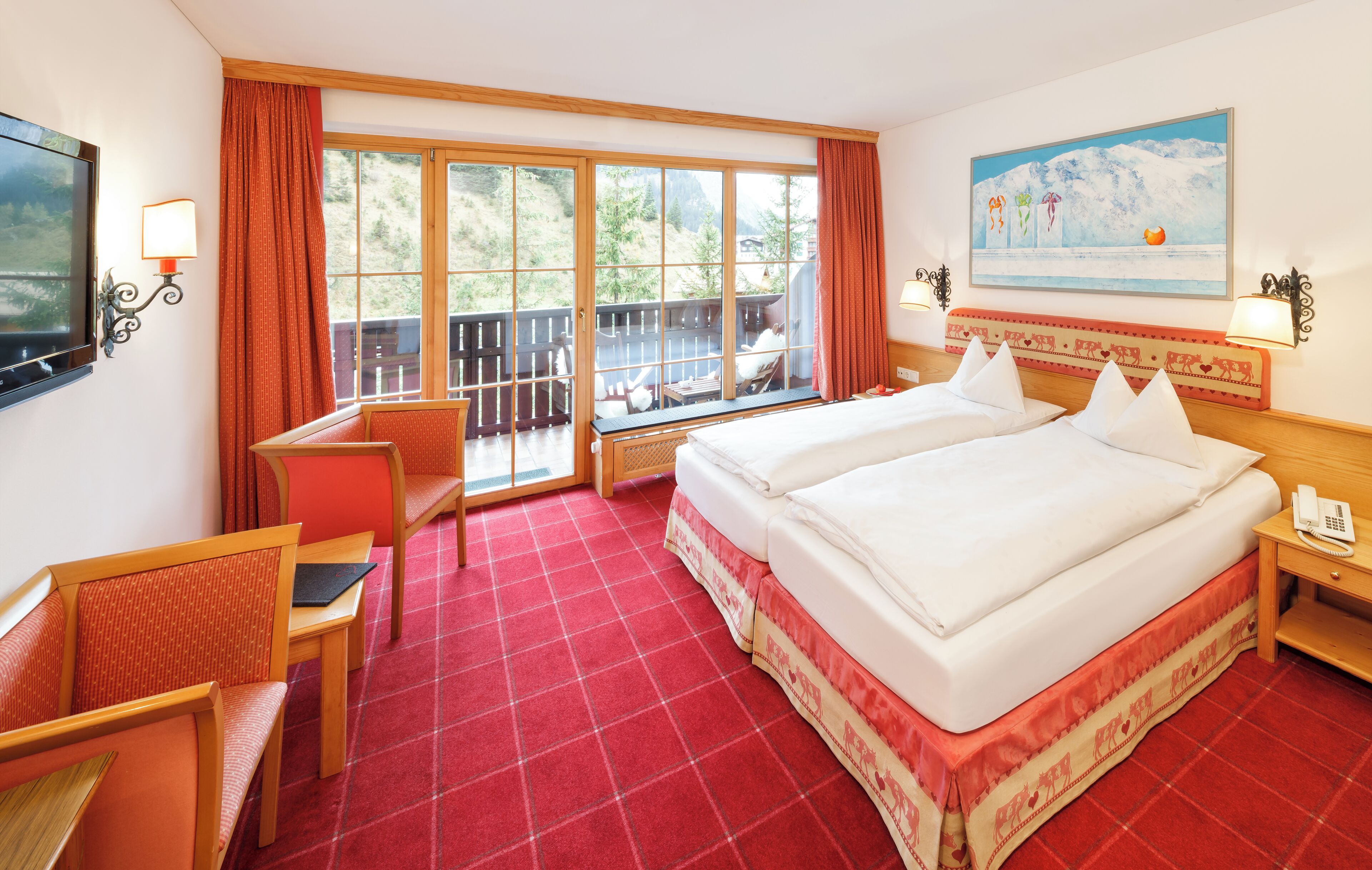 A hotel room with two beds, a desk, a chair, a TV, and a balcony with a view of trees and mountains.