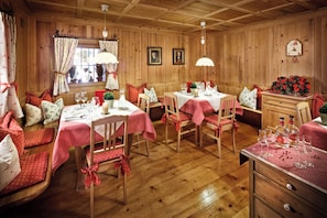 A cozy wooden dining room with tables set for a meal, featuring red and white tablecloths and matching chairs.