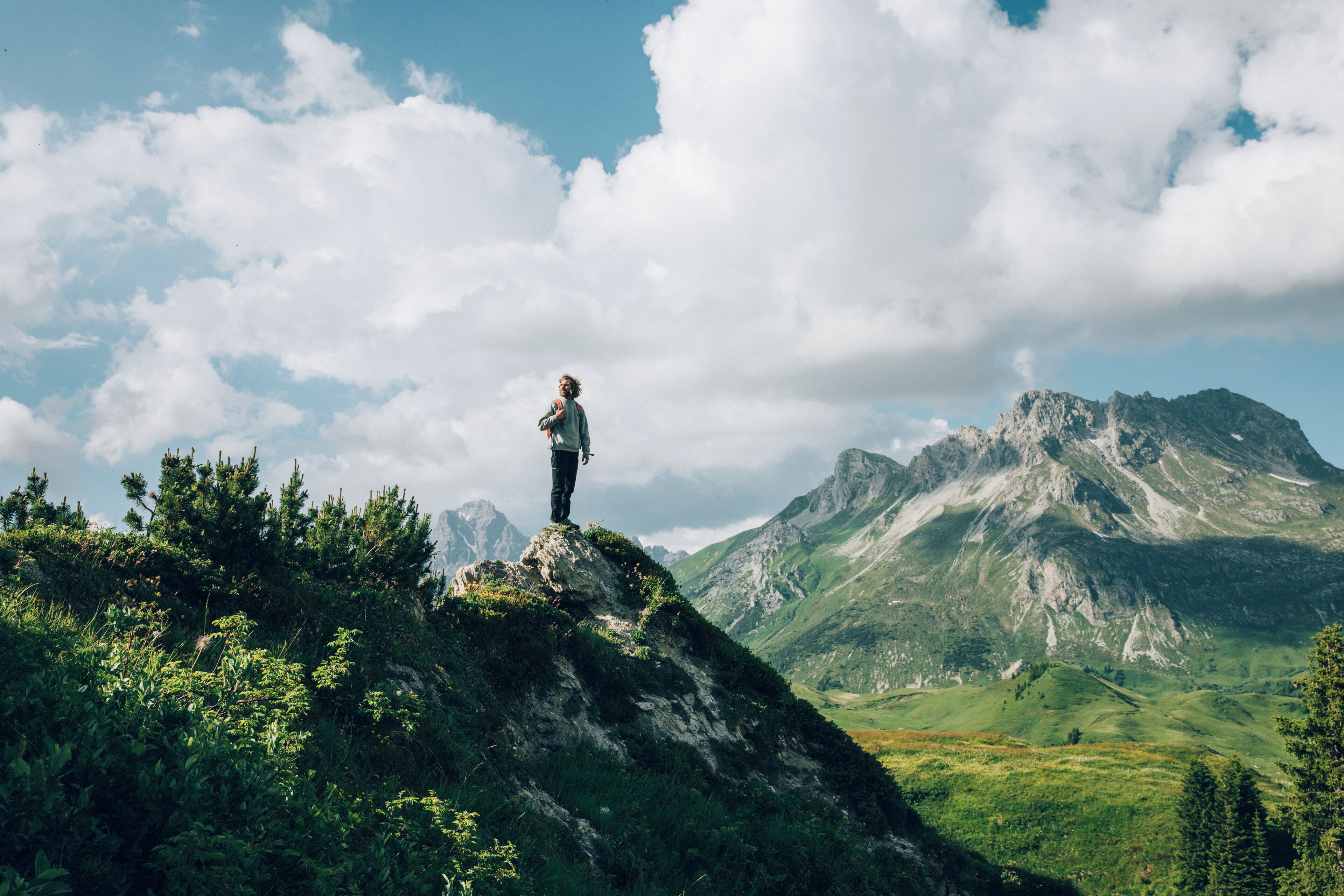 A person standing on a rocky outcrop with a mountainous landscape in the background.