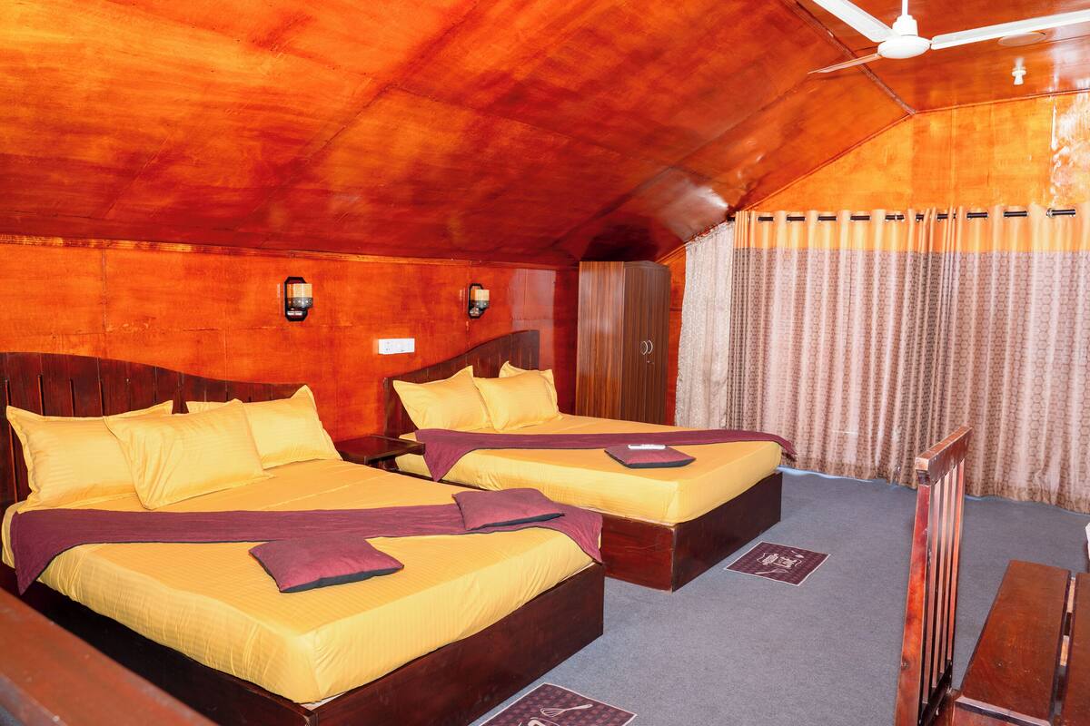 A room with two beds, wooden ceiling, and a ceiling fan.