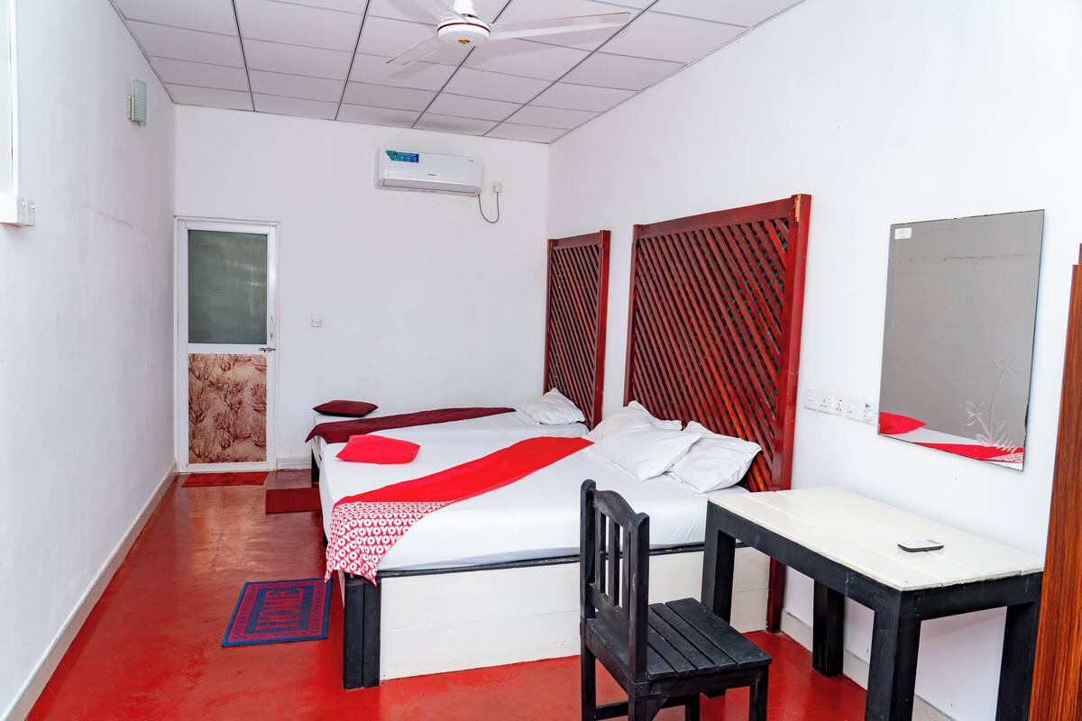 A hotel room with a bed, a desk, a chair, a mirror, and a red and white patterned rug.