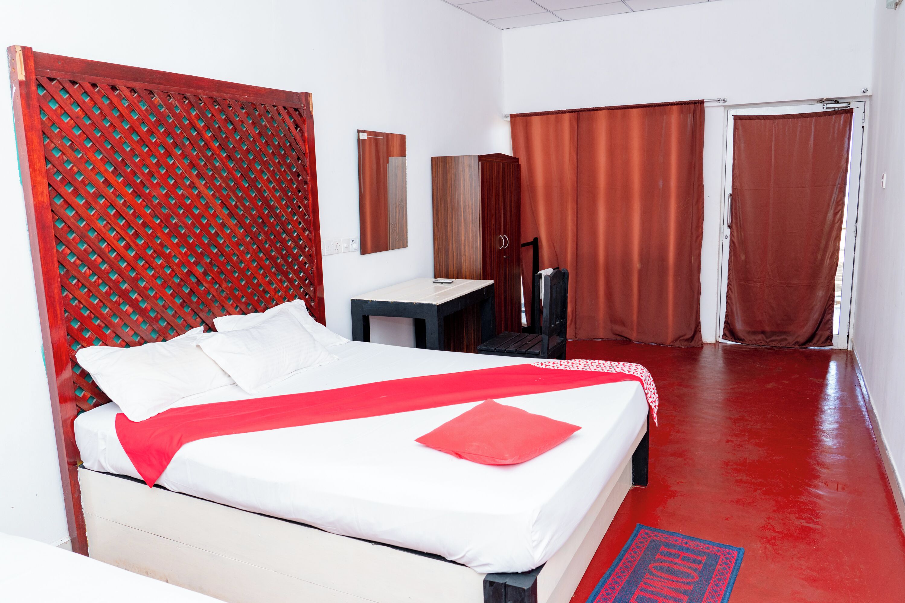 A hotel room with a bed, a desk, a mirror, and two doors.